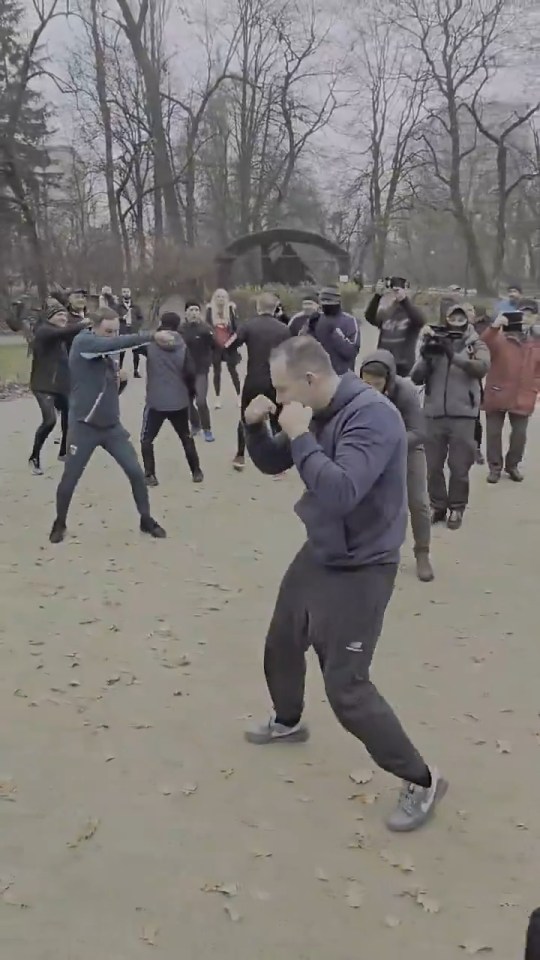 Man shadow boxing in a park with a crowd watching.