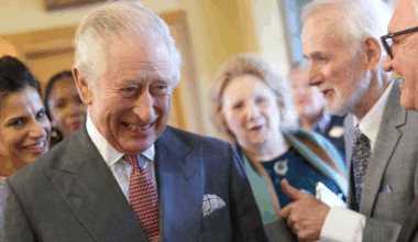 King Charles laughing in a gray suit and red tie