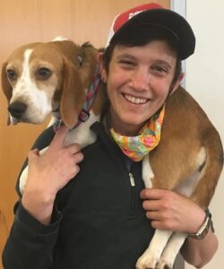 a veterinarian smiles at the camera with a Beagle wrapped around their shoulders, smiling and wearing a ball cap.