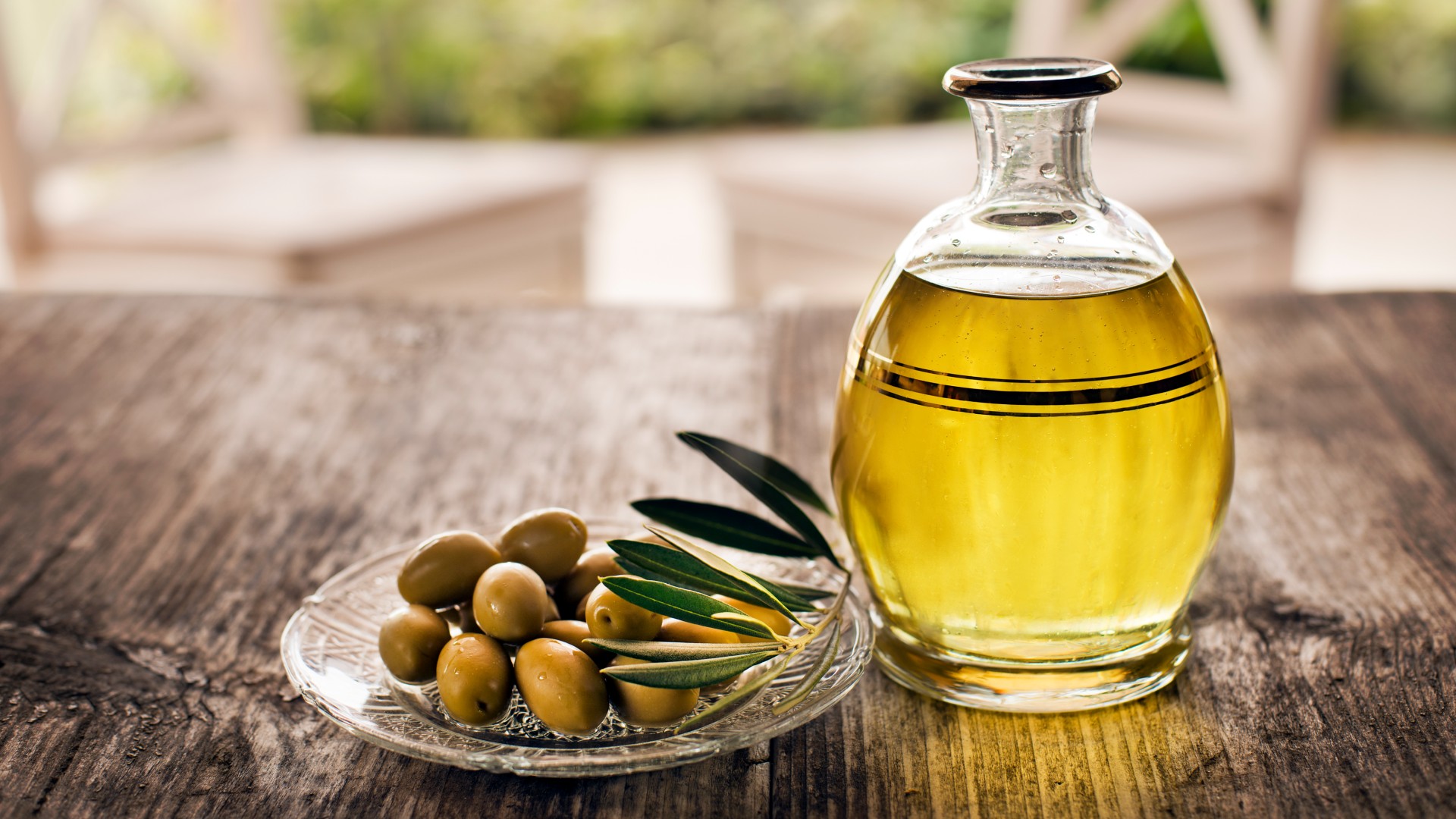 Jug of olive oil in a table next to a plate of olives