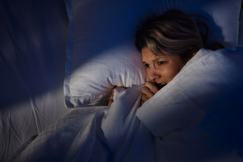 A blonde woman looking scared under a duvet