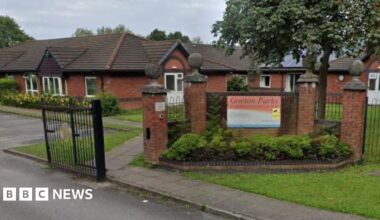 A sign for Gorton Parks Care Home hangs on a wall at the entrance to the nursing home complex. Red brick bungalows can be seen behind.