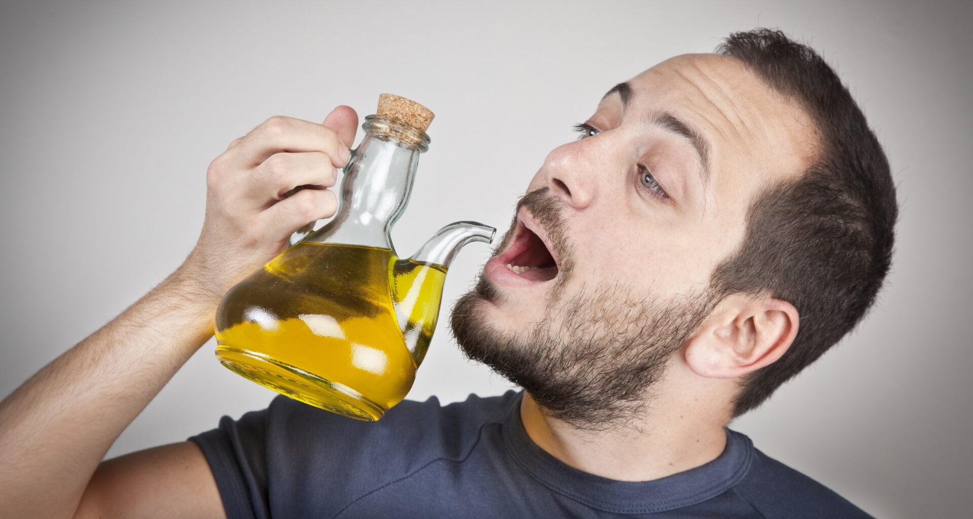 Man holding a jug of olive oil and pretending to drink from the spout