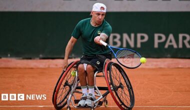 A man wearing black shorts and a green T-shirt, playing wheelchair tennis.