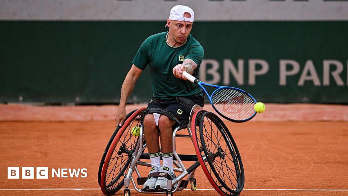 A man wearing black shorts and a green T-shirt, playing wheelchair tennis.