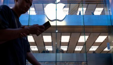 A pedestrian uses a smartphone while walking past an Apple store and logo in Hong Kong.