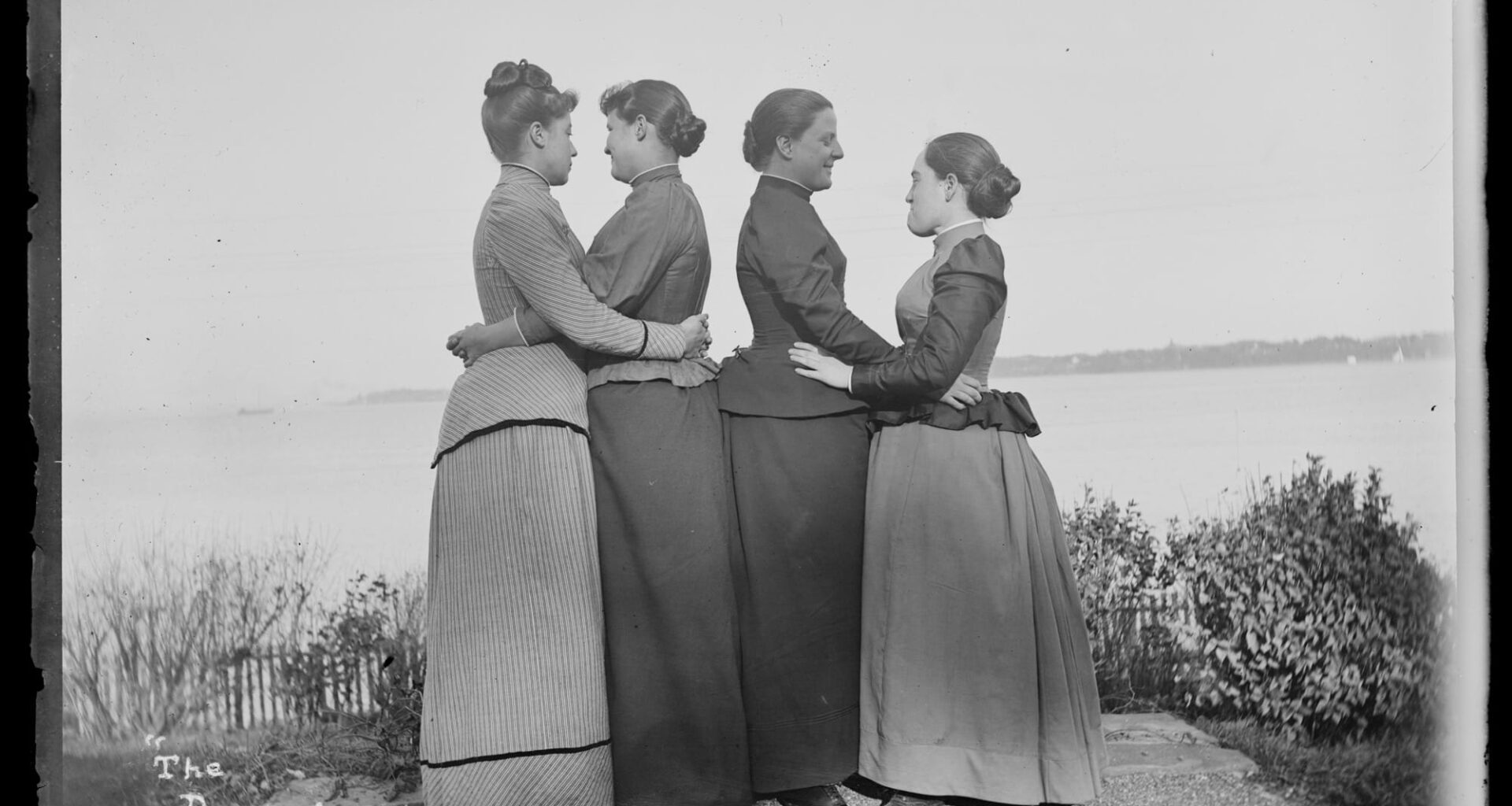 a black-and-white photo from the late 19th century of four women, turned to each other in twos and embracing