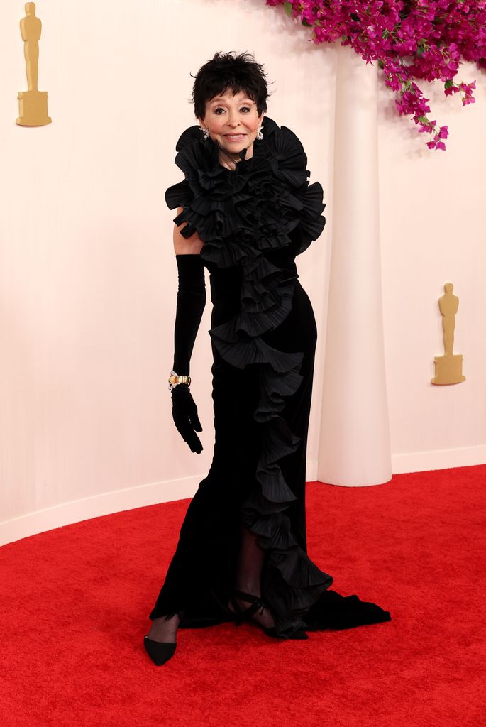Rita Moreno posing and smiling in a long, black ruffled dress