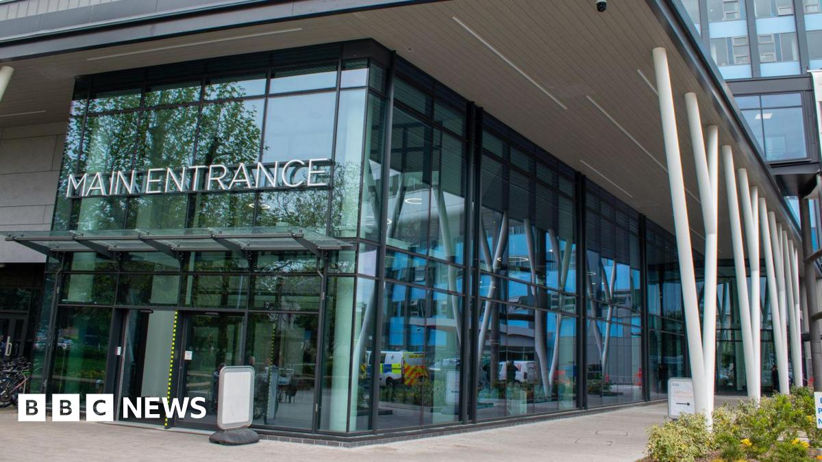 Large glass-fronted entrance to a modern building. There are white support beams and a sign which reads Main Entrance.