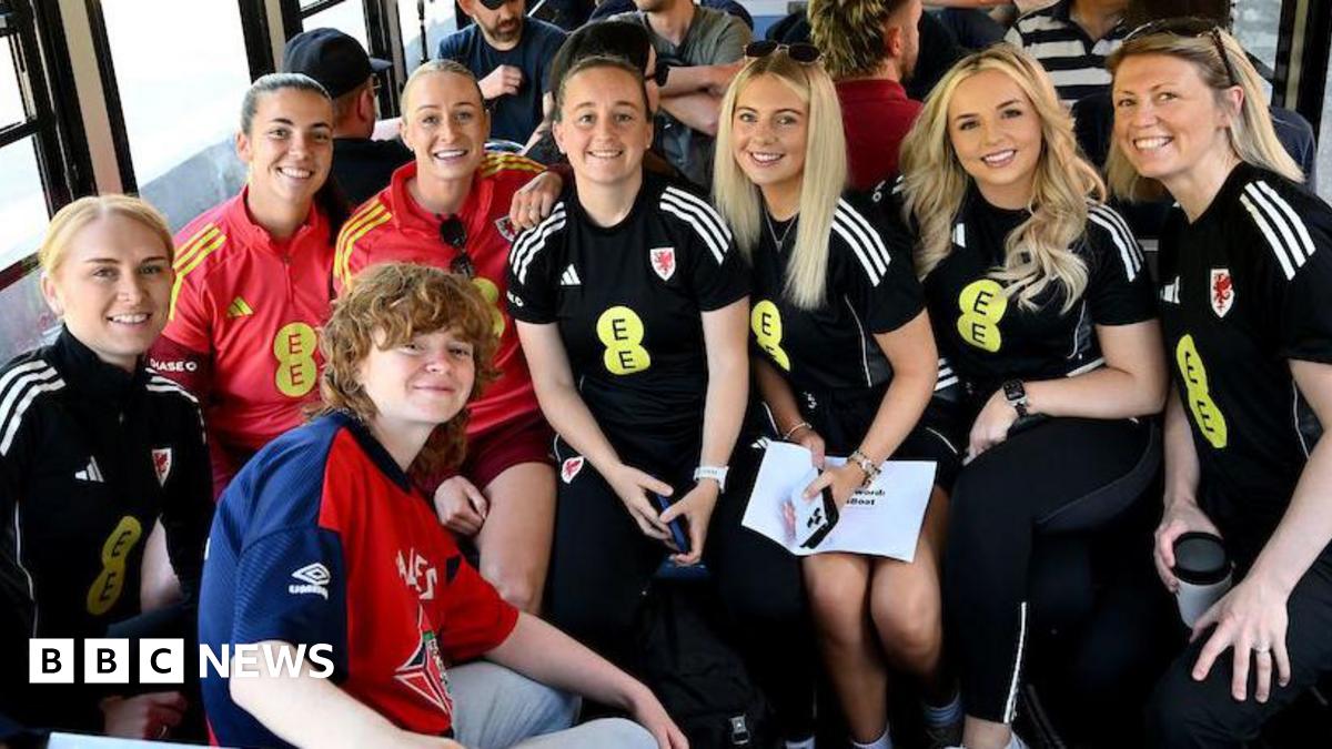 A group of women dressed in black and red football kits, all looking at the camera and smiling