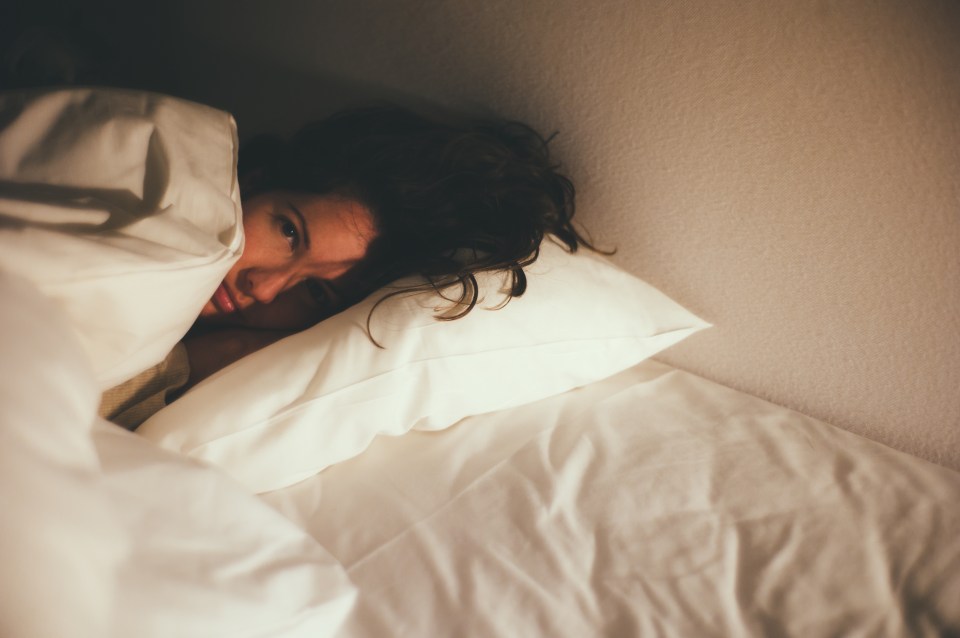Woman lying in bed, partially covered by blankets.