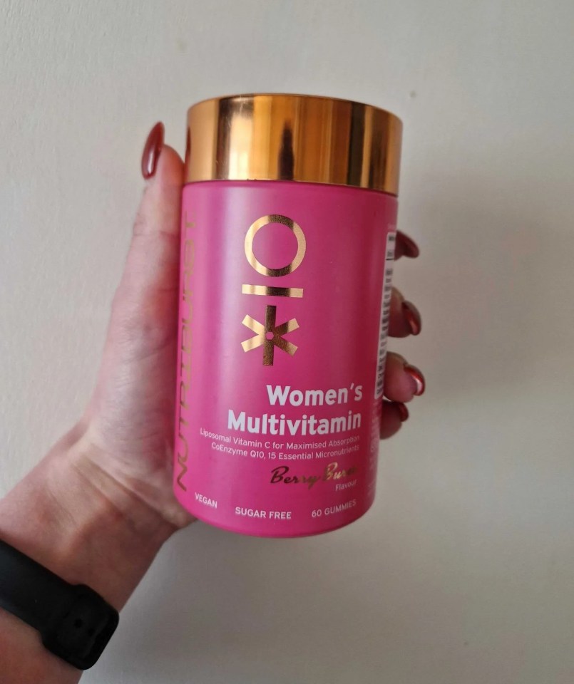Hand holding a pink jar of women's multivitamin gummies.