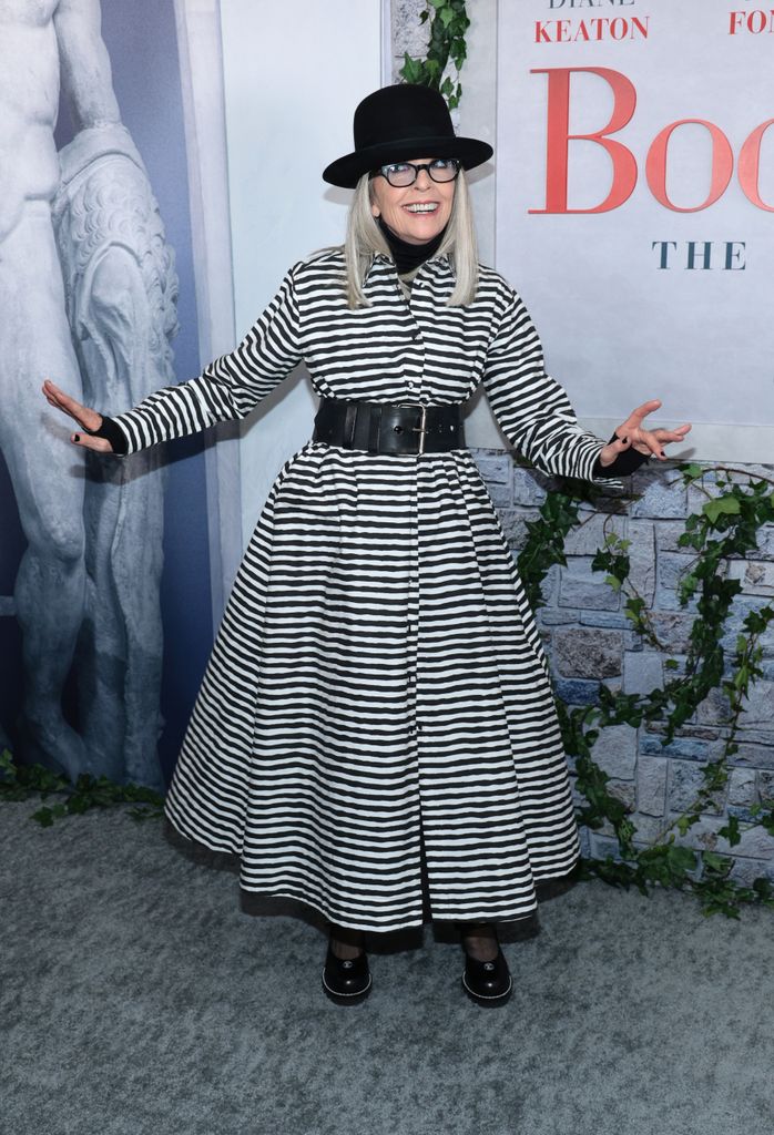 Diane Keaton smiling in a black and white striped dress with a hat on