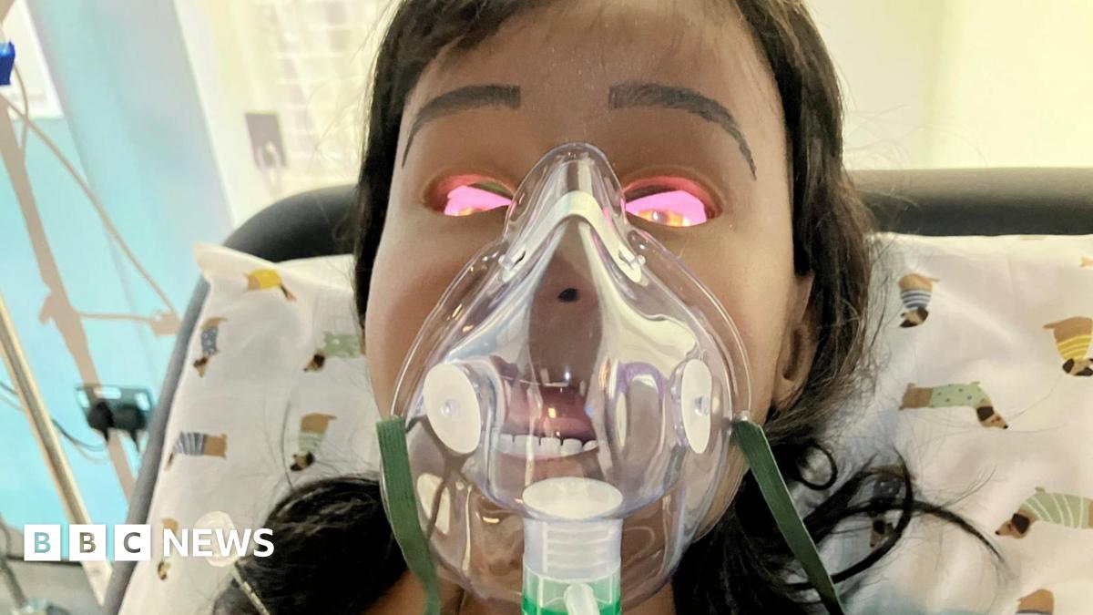 A manikin doll wearing an oxygen mask with brown hair leans back against a pillow