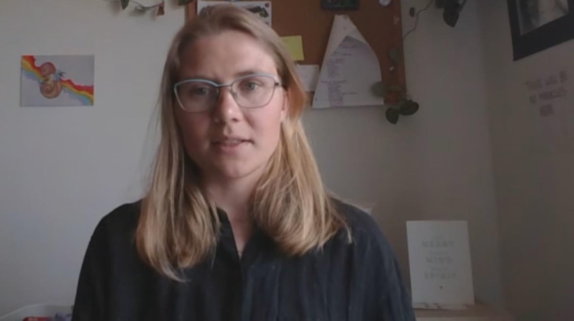 A blond woman speaks in a room with art behind her.