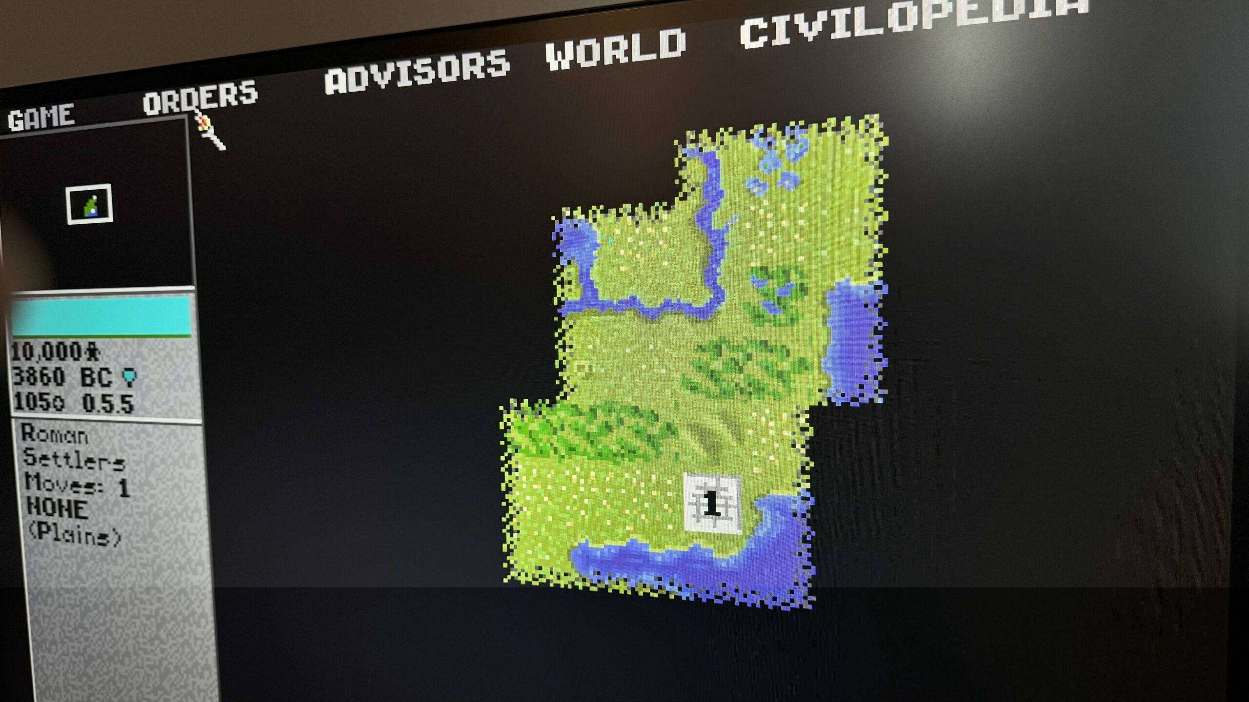 A picture of civilization 1 on a large flat screen monitor, showing a patch of green earth and blue water surrounded by black borders. 