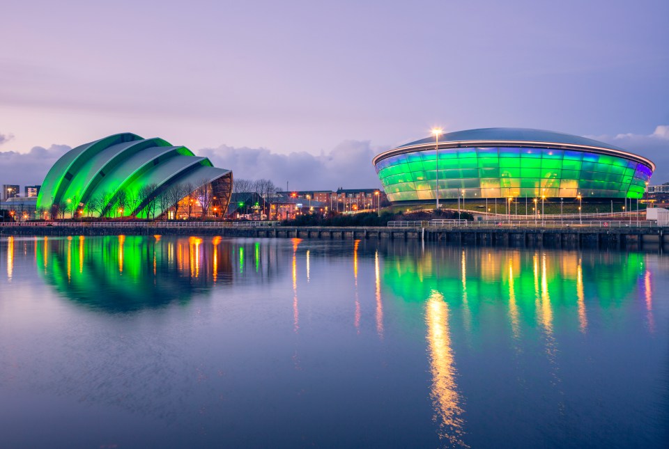 Glasgow's Armadillo and Scottish Hydro Arena lit up at night, reflected in the water.