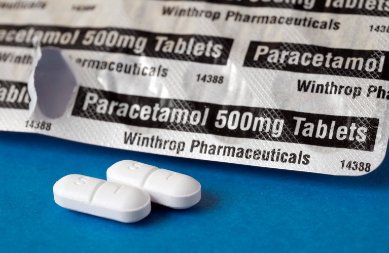 Blister pack of paracetamol tablets and two loose white tablets on a blue table.