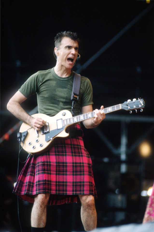 David Byrne playing guitar while wearing a kilt.