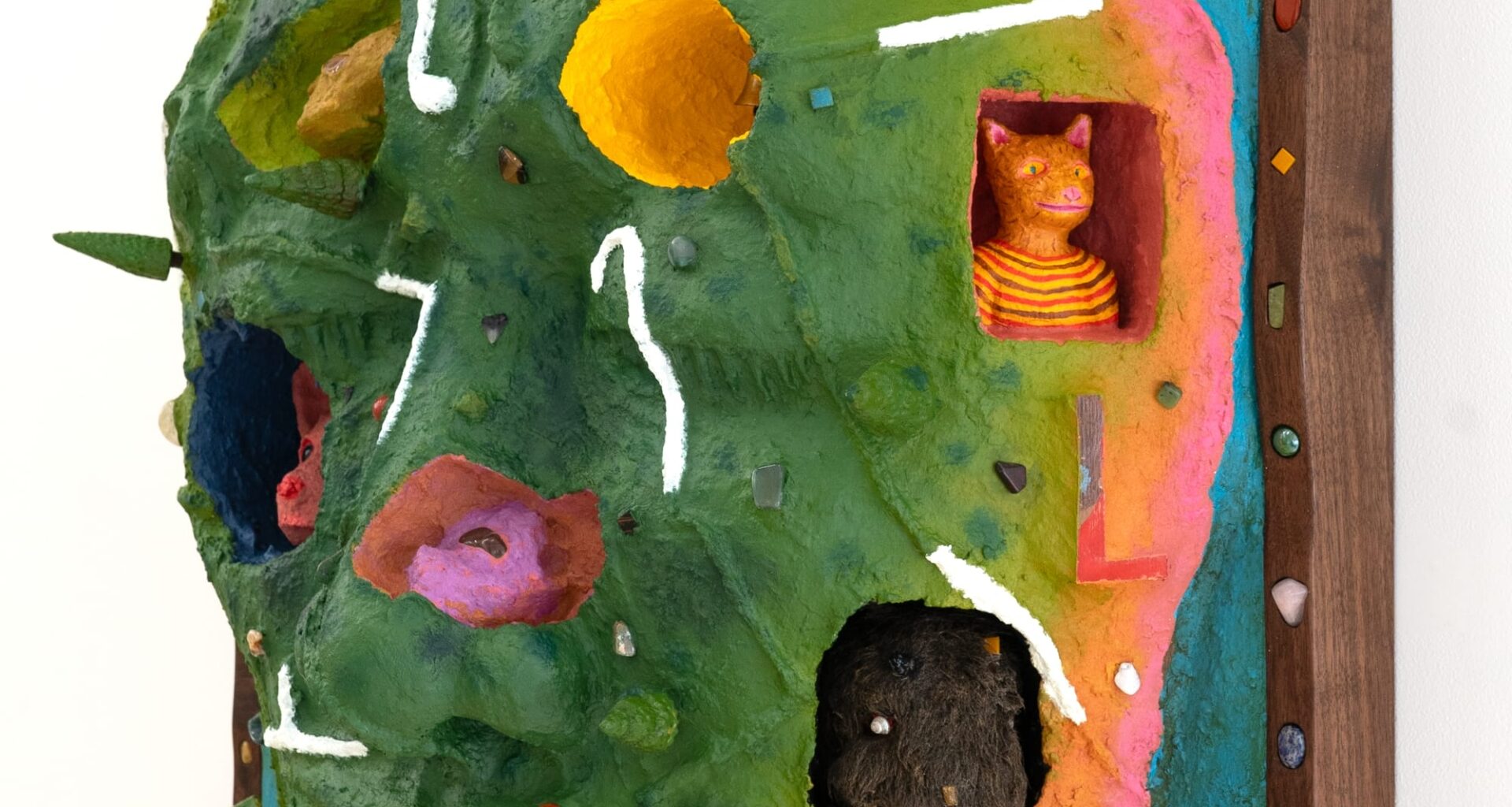 a side view of a wooly mammoth, pink animal, bell, and other objects embedded into a sculptural painting shaped like a face