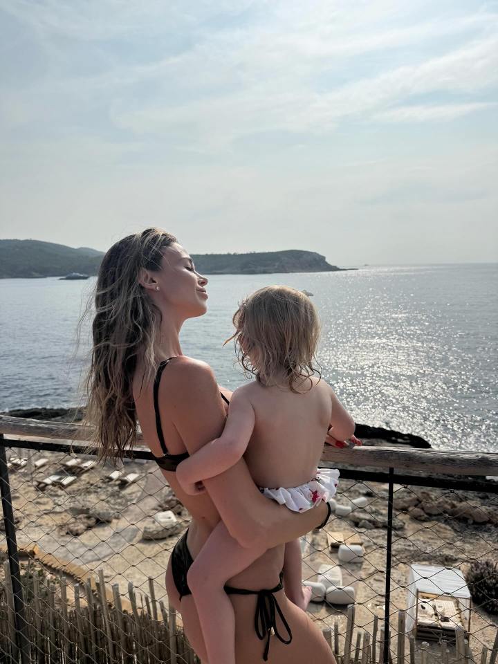Woman in bikini holding a toddler, overlooking the ocean.