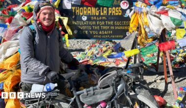 A man wearing a grey coat and black gloves is holding onto a bike and completing the Annapurna Circuit in Nepal.
