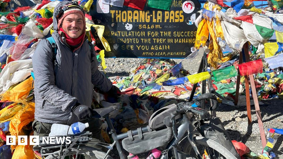 A man wearing a grey coat and black gloves is holding onto a bike and completing the Annapurna Circuit in Nepal.