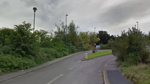 Google A road leading up to the entrance of the Reaside Clinic. There is a blue and white sign identifying the site.