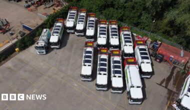 Dozens of white waste and recycling lorries parked on a large expanse of tarmac. Solar mats can be seen on the roof of each vehicle.