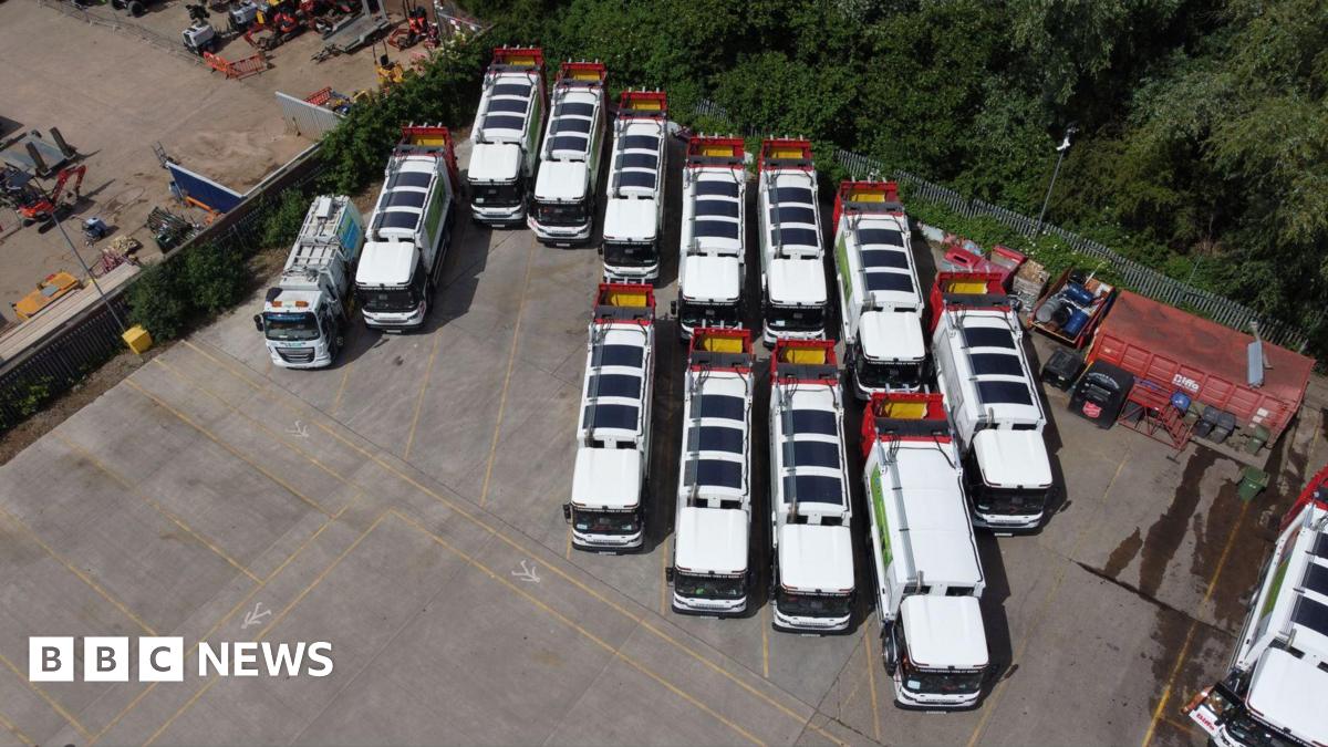 Dozens of white waste and recycling lorries parked on a large expanse of tarmac. Solar mats can be seen on the roof of each vehicle.