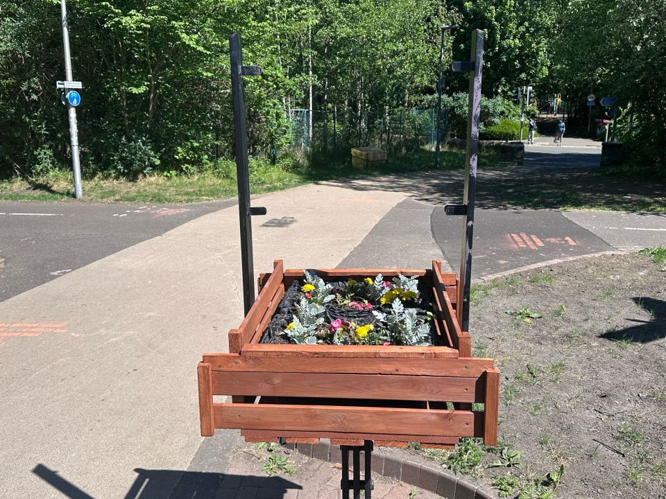Wooden planter box with flowers, mounted on a metal stand.