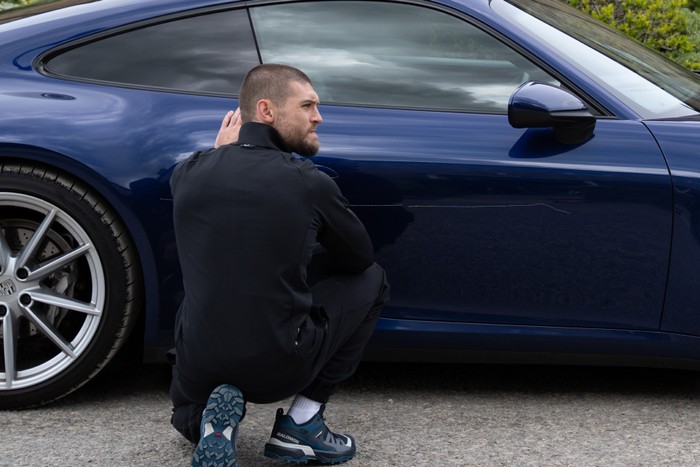 Joe crouching in front of a car in Emmerdale