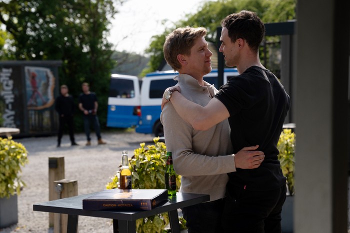 Aaron and John watching in the distance as Robert holds onto a man in Emmerdale