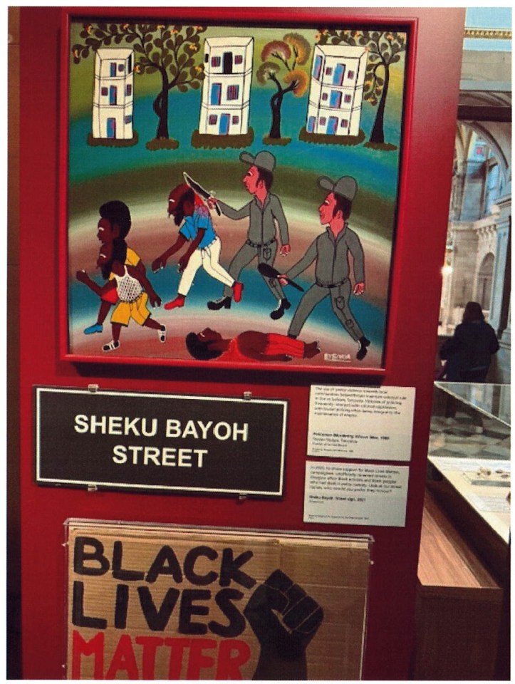 Illustration of police brutality, titled "Sheku Bayoh Street," displayed with a "Black Lives Matter" sign.
