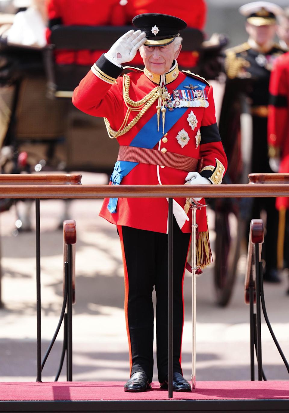 King Charles III gives a salute as he watches the parade march past after arriving back at Buckingham Palace after Trooping the Colour ceremony in central London (PA)