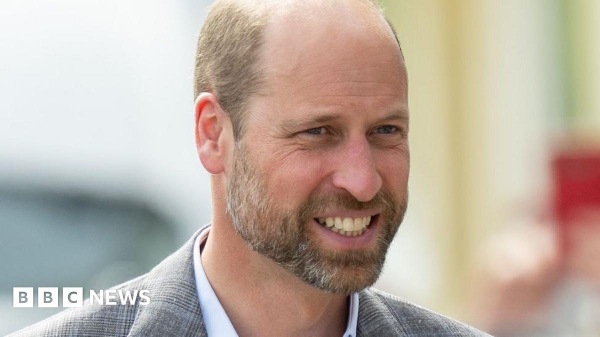 Prince William, the Prince of Wales, smiles as he is photographed arriving at an evening event. He wears a dinner jacket and bow tie with a white shirt. He has close-cropped hair and a short beard and moustache.