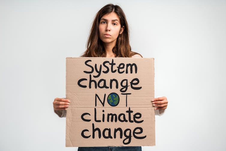 woman holds cardboard protest sign, system change not climate change