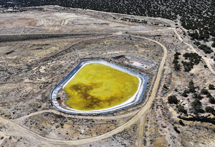 A stretch of barren land, marked by dirt roads around a bright yellow pond.