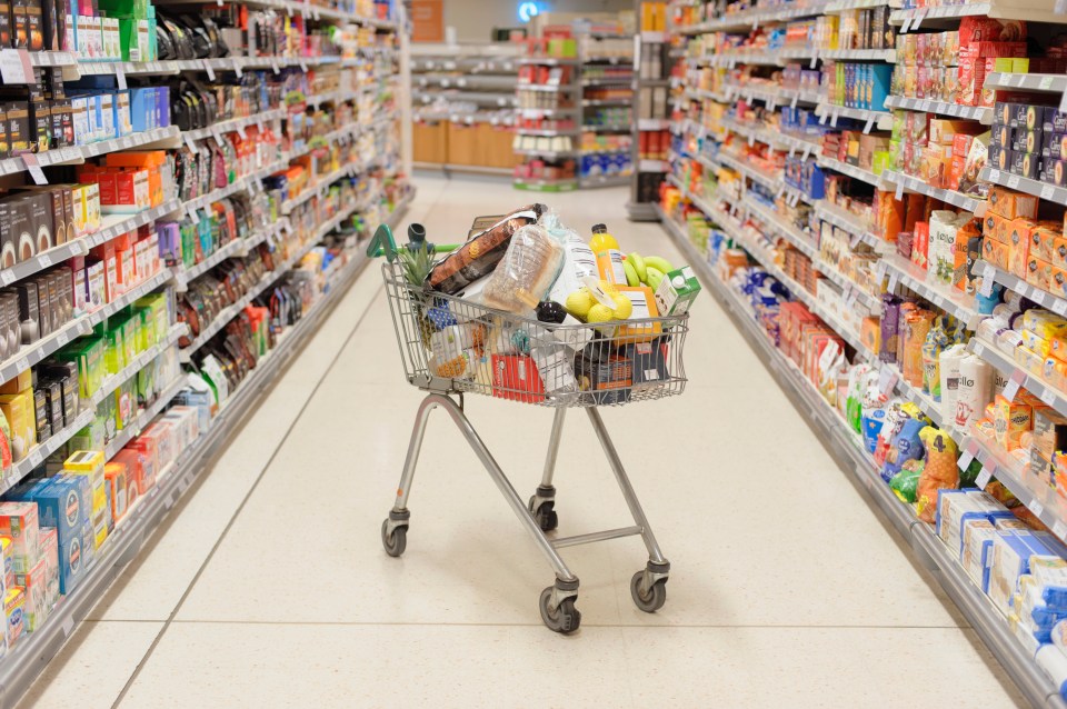 A shopping cart full of groceries in a supermarket aisle.
