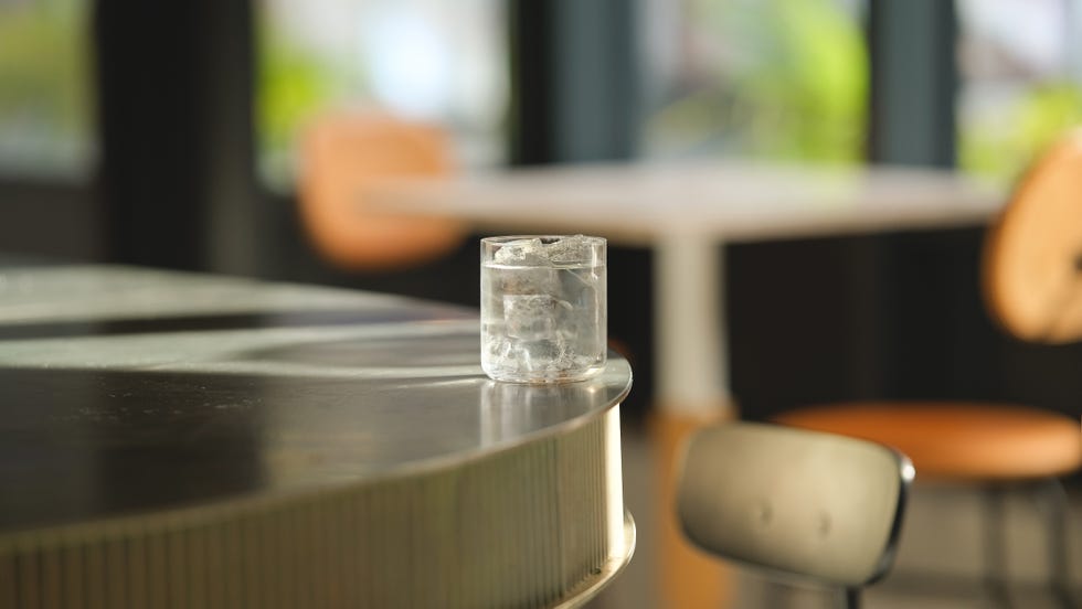 a clear glass with ice and margarita balancing on a bar edge