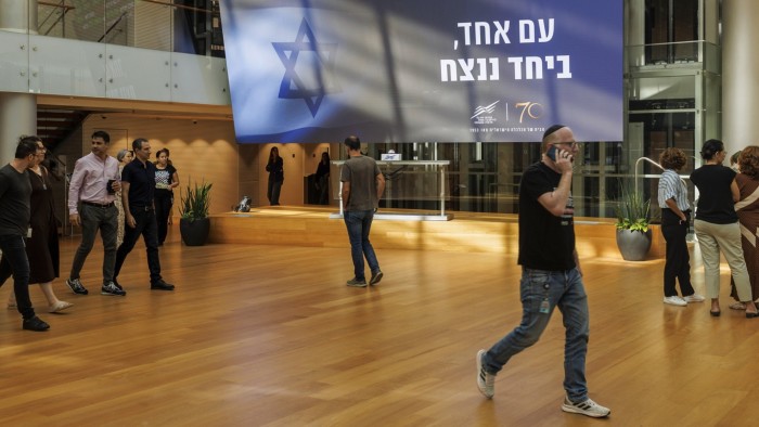 An electronic ticker displays stock price information above a sign reading ‘One Nation, Together We Will Win’ in the foyer of the Tel Aviv Stock Exchange