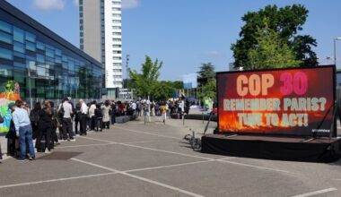 People stand in line as Greenpeace activists display a large screen saying “COP30 Remember Paris? Time to act!” in front of the Climate Change Conference in Bonn