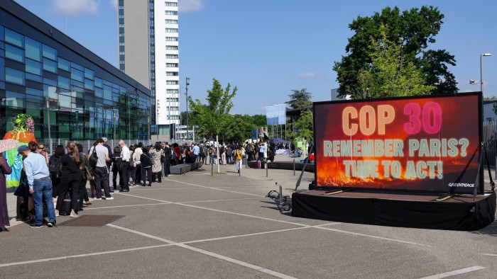 People stand in line as Greenpeace activists display a large screen saying “COP30 Remember Paris? Time to act!” in front of the Climate Change Conference in Bonn