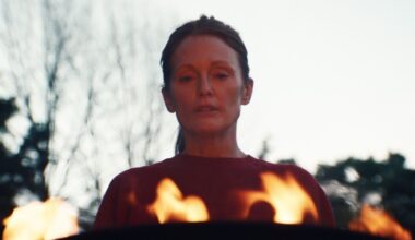 A woman stands facing us with flames in front of her
