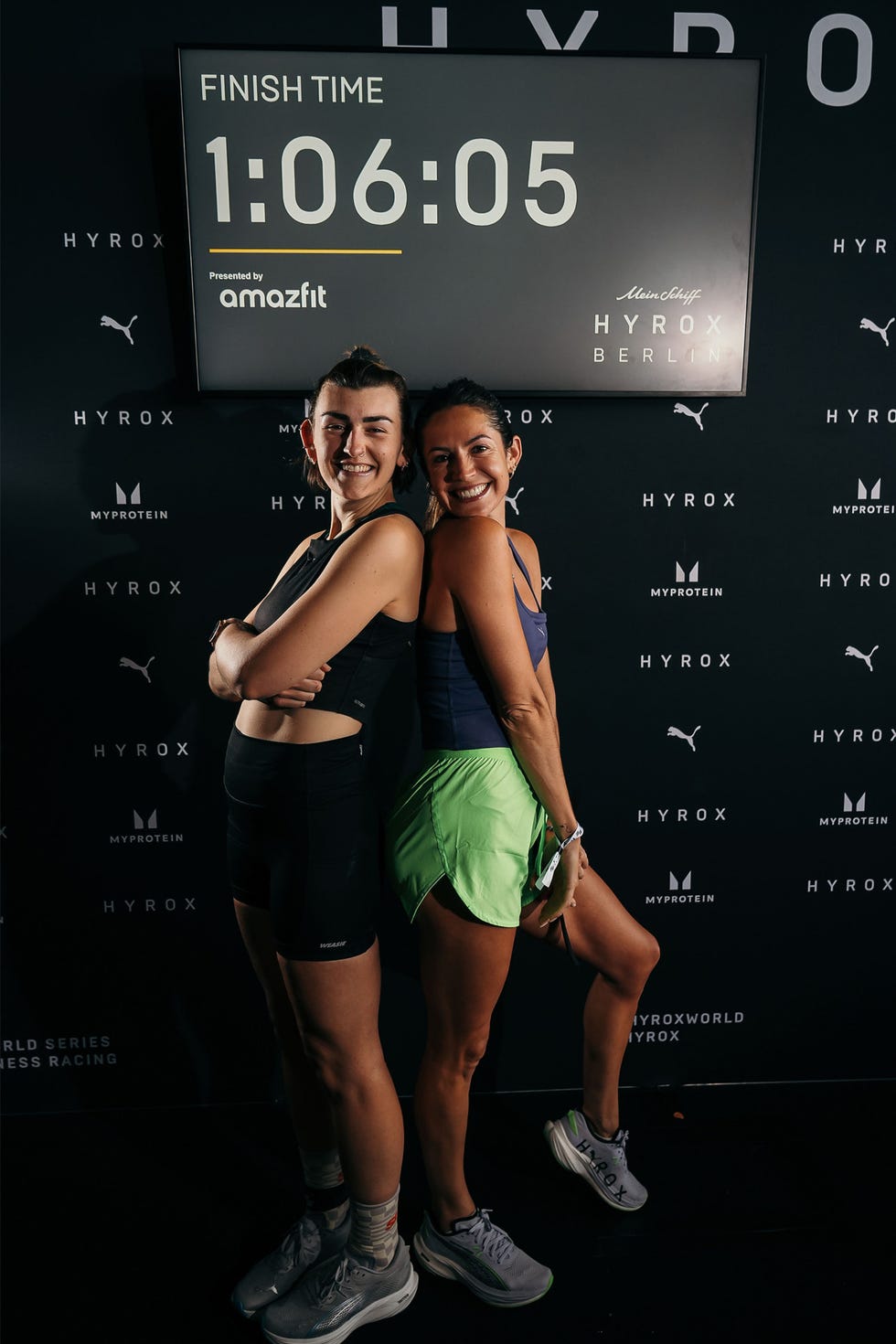 two women finishing a fitness competition under a sign displaying the time 1:06