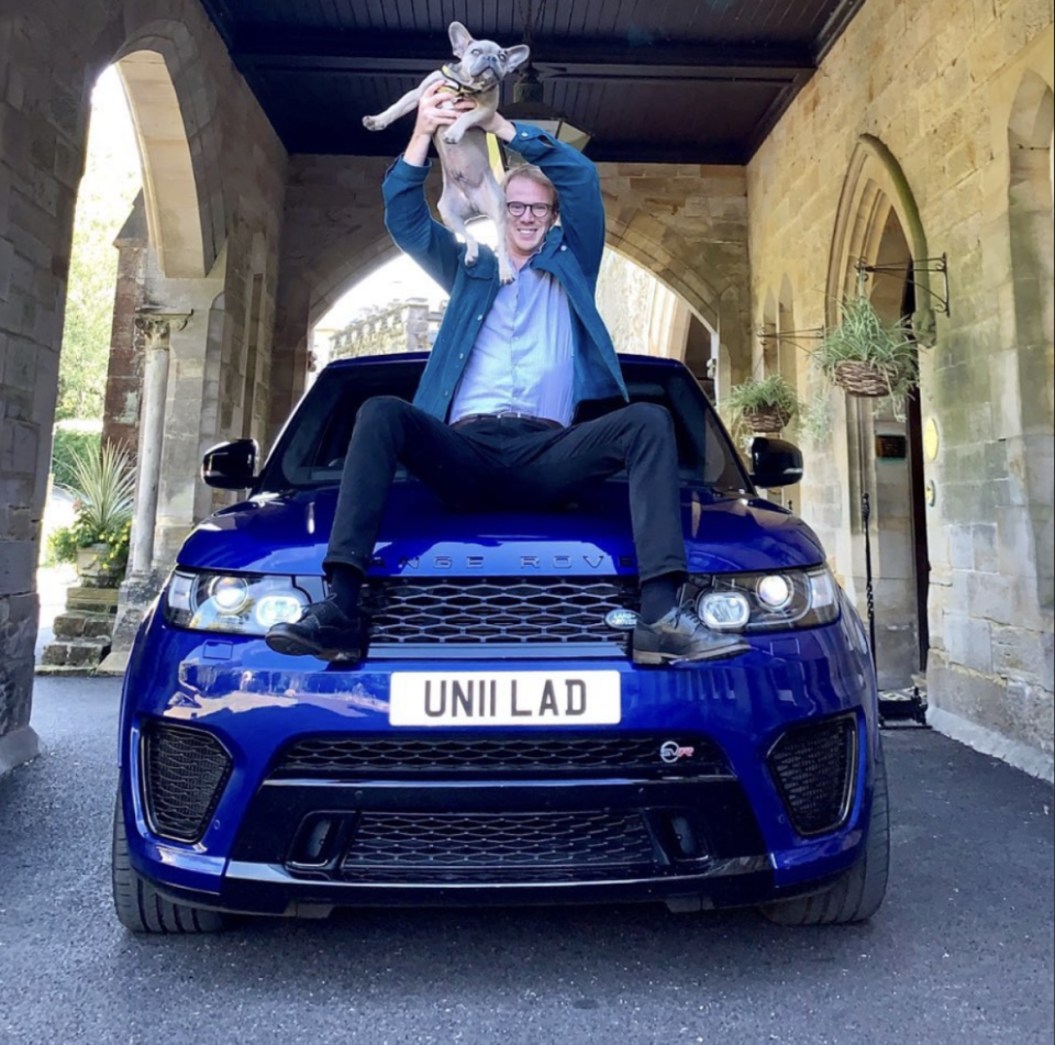 Man holding a dog sitting on the hood of a blue Range Rover.
