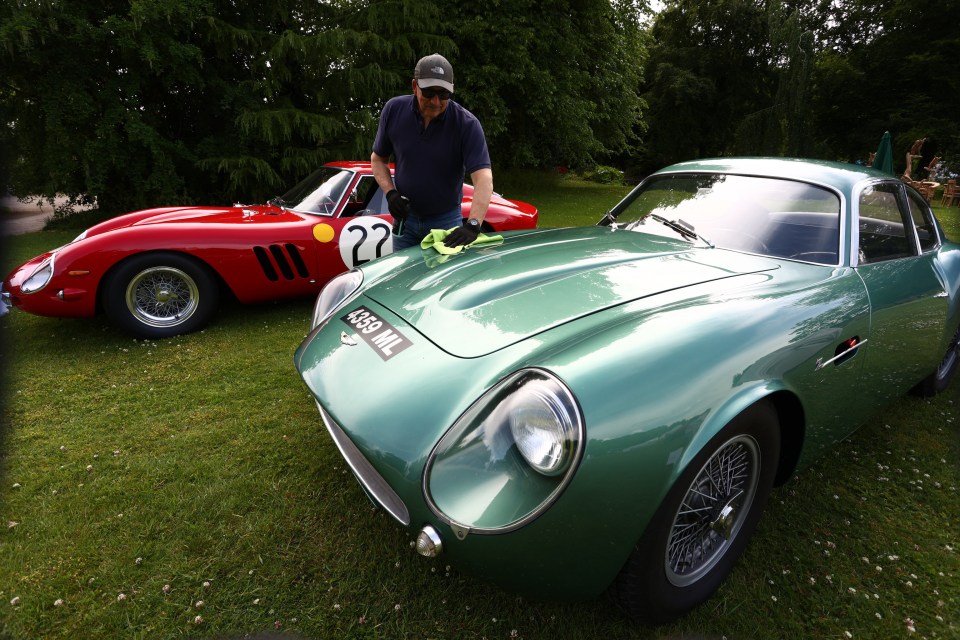 A man polishing a teal Aston Martin DB4GT Zagato and a red Ferrari 250 GTO.