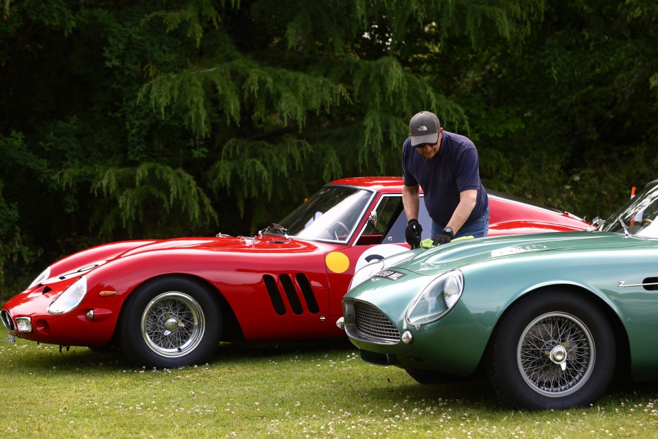A man cleaning a teal Aston Martin DB4 GT Zagato and a red Ferrari 250 GTO.