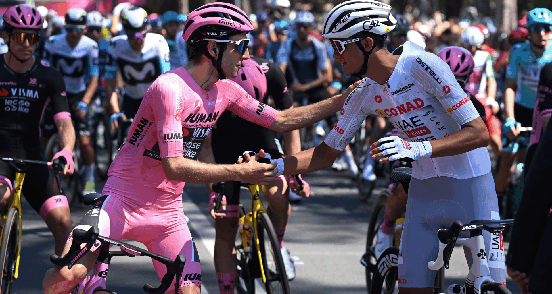 Simon Yates, wearing a full pink kit, shaking hands with Isaac del Toro