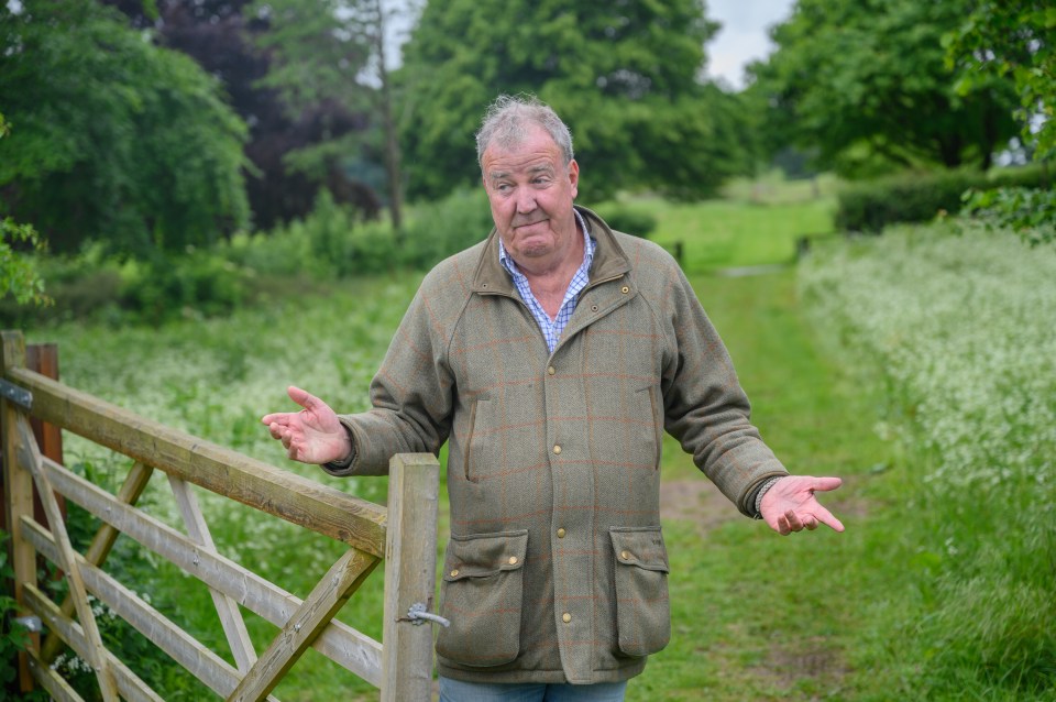Jeremy Clarkson from Jeremy Clarkson Farm season 4, standing by a gate with his arms outstretched.